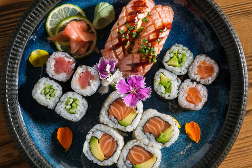 Top view of delicious assorted sushi rolls with raw salmon on plate with ginger wasabi and slices of lime on wooden table - ADSF46994