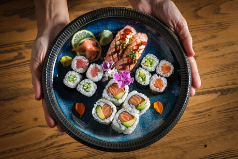 Top view of crop anonymous person holding plate with assorted tasty Japanese sushi rolls with raw fish and ginger with wasabi on slices of lime - ADSF46995