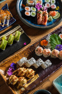 From above of tasty fresh sushi rolls with various toppings served on trays with decorative flowers on wooden table in cafe - ADSF47000