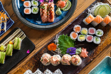 Von oben: verschiedene leckere Sushi-Rollen mit Fisch, serviert auf Tabletts mit Limettenscheiben und dekorativen frischen Blumen - ADSF47001