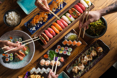 Von oben auf die Ernte unerkennbar Gruppe von Freunden essen frische Sushi mit Stäbchen beim Sitzen am Holztisch im Café - ADSF47004