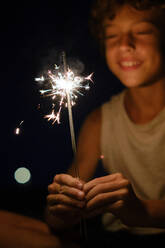 Fröhlicher, verschwommener Junge mit hellen, brennenden bengalischen Lichtern, der ein festliches Ereignis bei Nacht feiert - ADSF47014