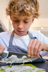 Crop focused child with wavy hair and knife chopping fresh onion while cooking at home - ADSF47016