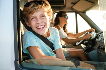 Side view of preteen boy laughing happily while traveling with mother in car and looking out of opened window during summer holidays - ADSF47026