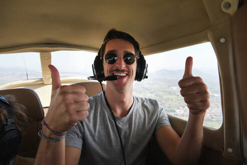 Stockfoto eines glücklichen Mannes, der ein Headset für die Luftfahrt trägt, eine Tour mit einem Leichtflugzeug genießt und in die Kamera schaut. - ADSF47036