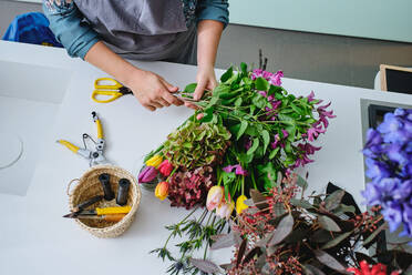 Von oben der Ernte anonyme weibliche Floristin in Schürze Schneiden von Stielen und die Schaffung von Bouquet von sortierten Blumen, während am Tisch in Blumenladen sitzen - ADSF47061