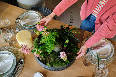 From above of unrecognizable housewife placing ceramic flowerpot with planted hyacinths on table while serving table for lunch in modern kitchen at home - ADSF47065