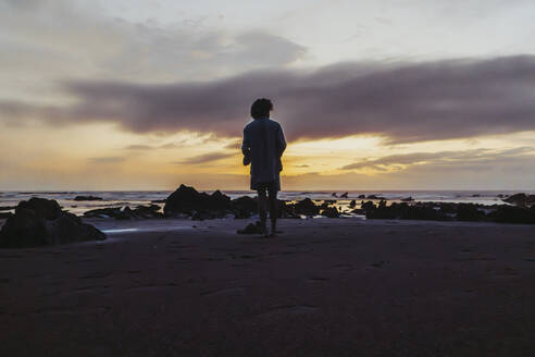 Mann schaut am Strand stehend aufs Meer - PBTF00251