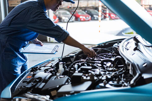 Car mechanic holding clipboard and checking to maintenance vehicle by customer claim order in auto repair shop garage. Engine repair service. People occupation and business job. Automobile technician - INGF12087