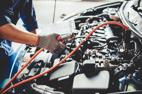 Car mechanic holding battery electricity trough cables jumper and checking to maintenance vehicle by customer claim order in auto repair shop garage. Repair service. People occupation and business job - INGF12089