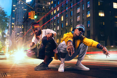 Two black rappers dancing on city street, car lights exposure effect. Rap performers against cityscape, underground music lifestyle, urban style - INGF12105