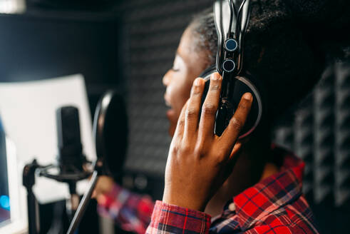 Young woman in headphones songs in audio recording studio. Musician listens composition, professional music mixing. Young woman songs in audio recording studio - INGF12114