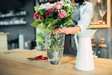 Female florist making flowers arrangement on the table in shop. Floral artist decorates bouquet at the workplace. Florist making flowers arrangement in shop - INGF12120