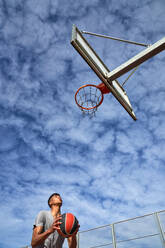 Niedriger Blickwinkel eines männlichen Basketballspielers, der auf den Ring schaut und sich darauf vorbereitet, den Ball in den Korb zu werfen, im Sommer - ADSF47098