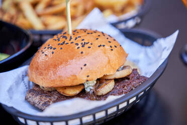 Closeup hohen Winkel der appetitlich saftigen Burger mit Gemüse und Fleisch auf Korbwaren Platte platziert und serviert mit Pommes frites auf dem Tisch - ADSF47108