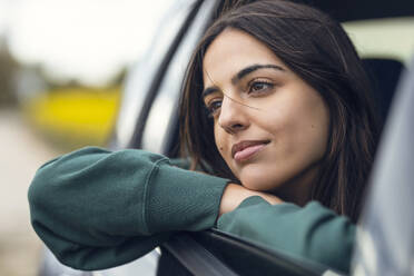 Thoughtful young woman leaning on electric car window - JSRF02611