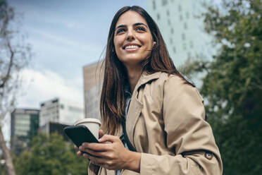 Happy woman with coffee cup and smart phone in city - JSRF02620