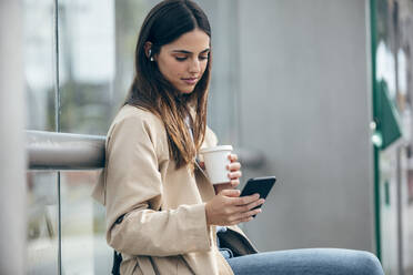 Young woman with coffee cup using smart phone - JSRF02623