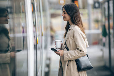 Smiling young woman standing with smart phone near train - JSRF02627