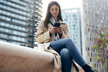 Lächelnde Frau mit Mobiltelefon vor einem Gebäude - JSRF02634