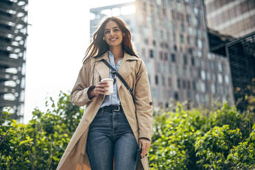 Lächelnde Frau mit Kaffeetasse vor einem Gebäude - JSRF02637