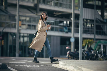 Junge Frau mit Smartphone und Kaffeetasse auf der Straße - JSRF02644