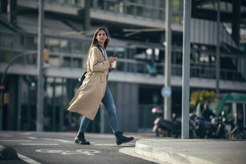 Junge Frau mit Smartphone und Kaffeetasse auf der Straße - JSRF02644