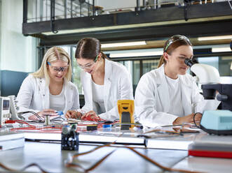 Junge Ingenieure messen mit dem Multimeter und ein Kollege untersucht mit dem Mikroskop - CVF02500