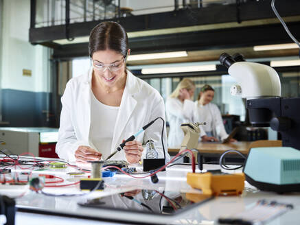 Glücklicher Ingenieur, der eine Leiterplatte mit einem Multimeter untersucht und misst - CVF02501