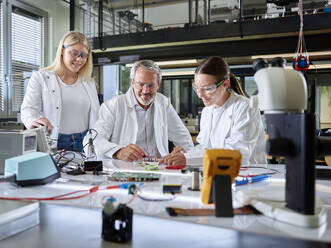 Smiling professor teaching trainees over circuit board in laboratory - CVF02506