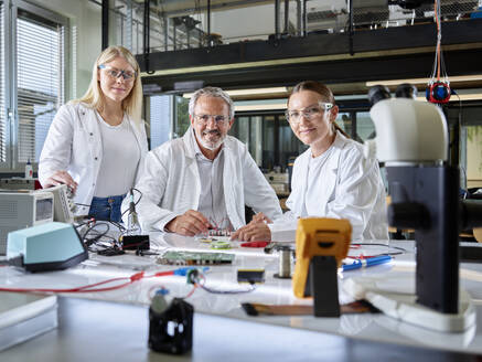 Smiling engineers with equipment on workbench in laboratory - CVF02507