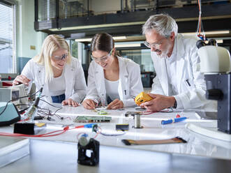 Zufriedener Professor mit Auszubildenden bei der Arbeit an einer Leiterplatte im Labor - CVF02509