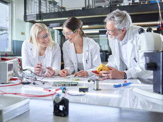 Smiling professor with trainees working on circuit board in laboratory - CVF02510