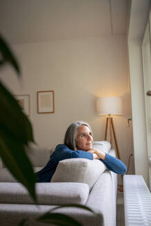 Nachdenkliche reife Frau sitzt zu Hause auf dem Sofa - KNSF09834