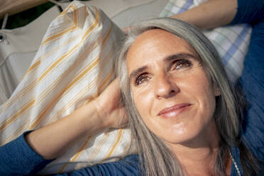 Lächelnde Frau mit grauem Haar entspannt sich an einem sonnigen Tag - KNSF09857