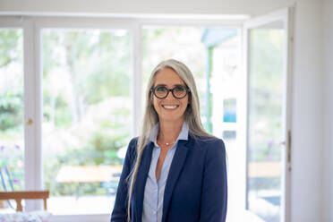 Happy businesswoman wearing eyeglasses at home - KNSF09859