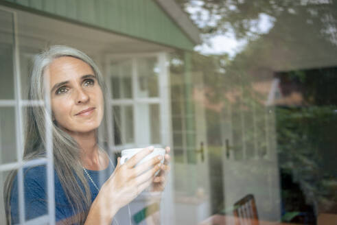 Lächelnde Frau mit Teetasse durch Glas gesehen - KNSF09861