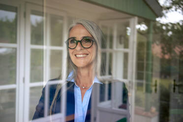 Happy businesswoman with gray hair seen through glass - KNSF09865