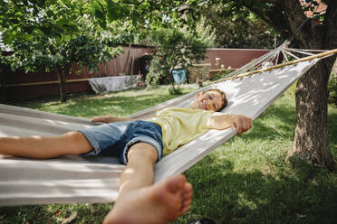 Fröhlicher Junge entspannt sich in der Hängematte im Hinterhof - NLAF00137