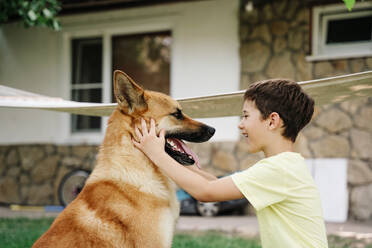 Happy boy stroking dog in back yard - NLAF00143