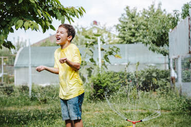 Happy boy playing with water splashing from hose - NLAF00145