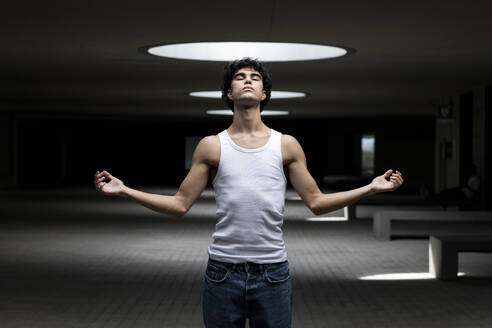 Young man with eyes closed and arms raised standing in parking lot - LMCF00545