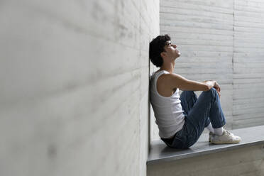 Young man with eyes closed sitting on wall - LMCF00548