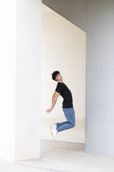 Young man jumping in front of white wall - LMCF00554