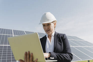 Ingenieur mit Schutzhelm bei der Arbeit an einem Laptop vor einer Solaranlage - OSF02149