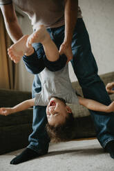 Father carrying son upside down at home - ANAF02134