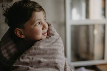 Nachdenklicher Junge, eingewickelt in eine Decke, zu Hause - ANAF02140