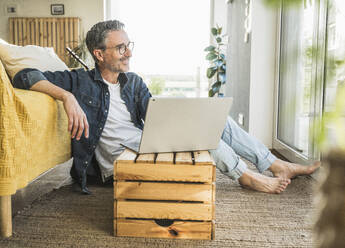 Lächelnder reifer Freiberufler mit Laptop, der zu Hause sitzt - UUF30259