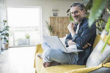 Smiling businessman doing video call on laptop sitting at home - UUF30266