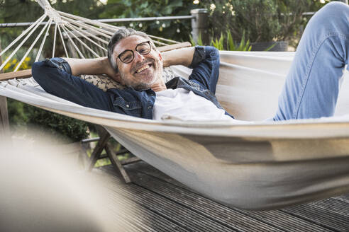 Lächelnder Mann mit Brille entspannt sich in der Hängematte - UUF30273